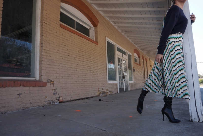 a woman in a printed pleated skirt, sweater and boots on a sidewalk