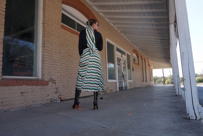 a woman in a pleated printed skirt and sweater and boots