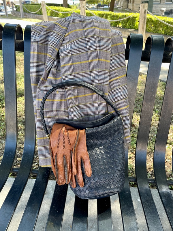 a plaid blazer, navy bucket bag and brown gloves on a bench 
