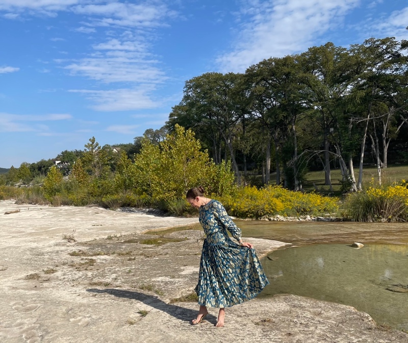 a woman in a teal and gold lame dress on rocks by a lake