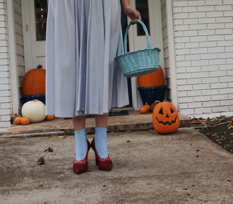 a woman with pumpkins in ruby red slippers and blue socks and blue and white dress