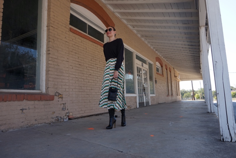 a woman in a pleated printed skirt and sweater and boots