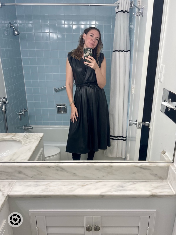 a woman in a black leather dress in a bathroom mirror