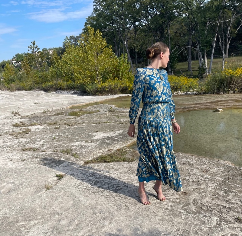 a woman in a teal and gold lame midi dress on rocks by a lake