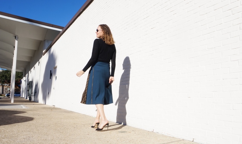 a woman in a blue wool skirt with a black sweater and heels q