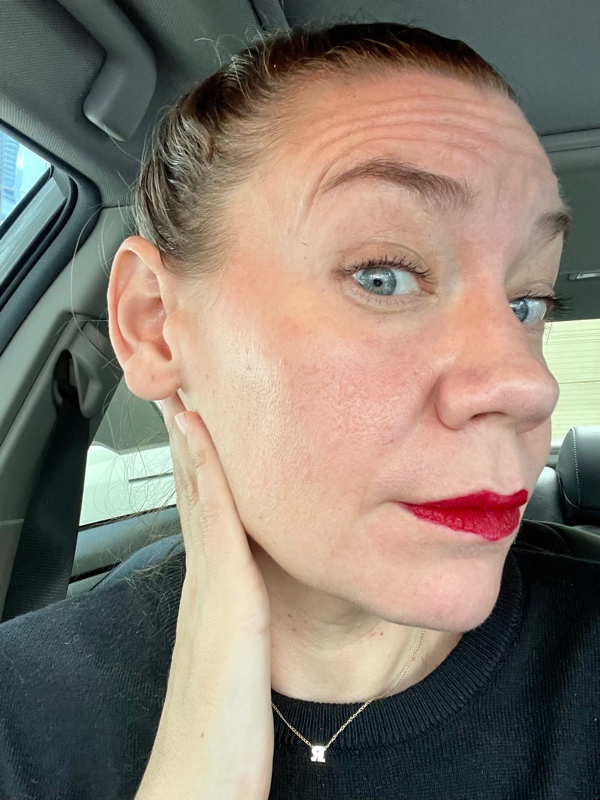 a woman with a bun and red lipstick taking a selfie in a car