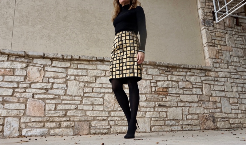 a woman in black turtleneck, hose and heels and a golden tile skirt