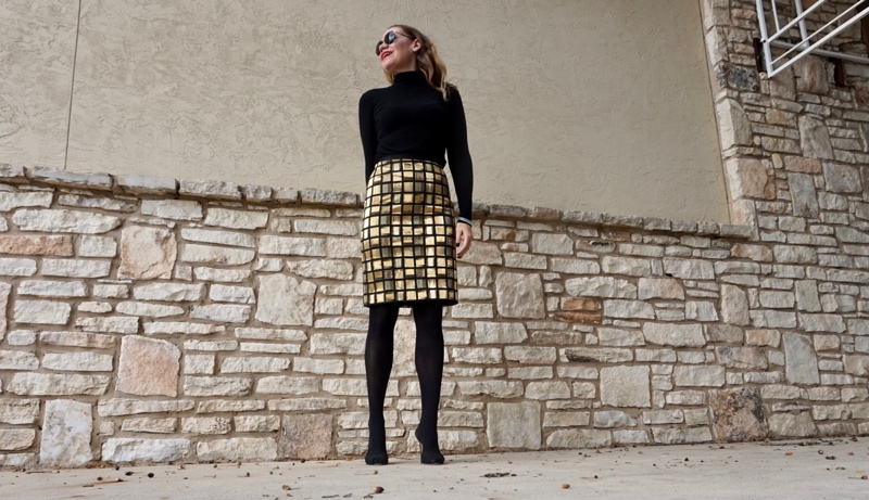 a woman in a black turtleneck, hose and a gold skirt