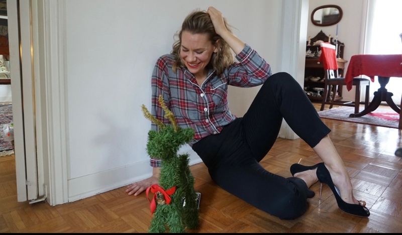 a woman sits in a plaid shirt and black pants by a green reindeer
