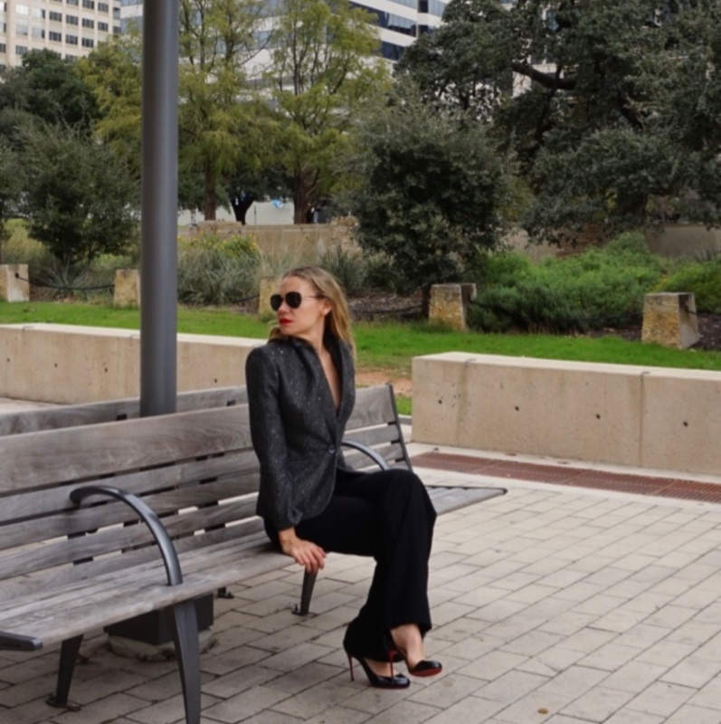 a woman in a grey blazer and black pants on a bench