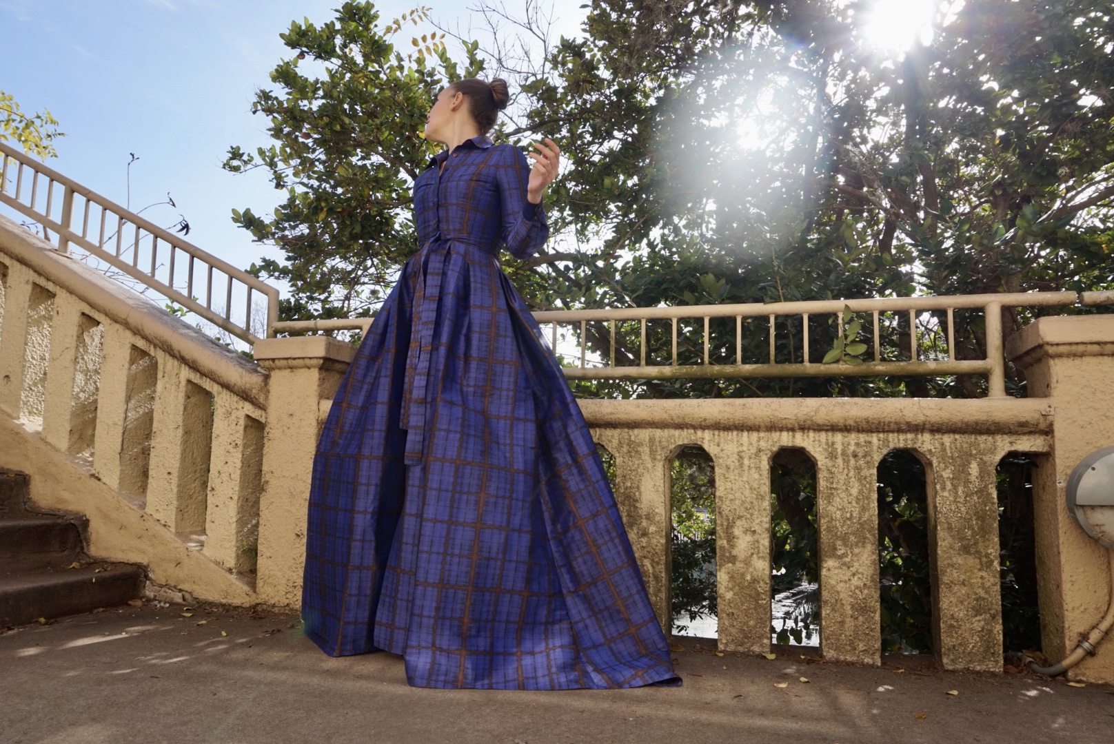 a woman in a plaid purple gown and shoes in front of stone wall and trees