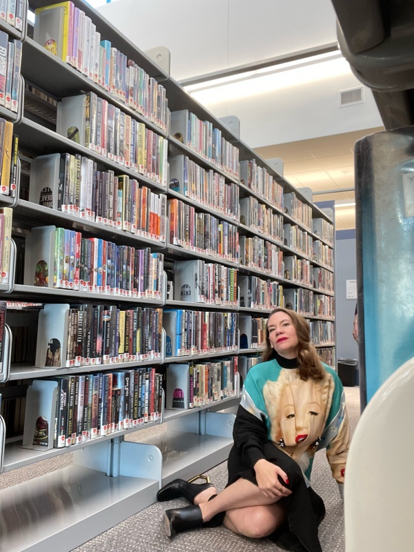 a woman sitting in library stacks wearing a black dress with the face of Marilyn Monroe on it