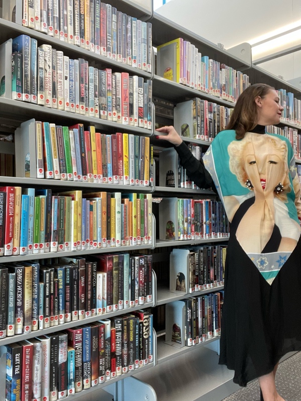 a woman in dress whit eh face of Marilyn Monroe in library stacks 
