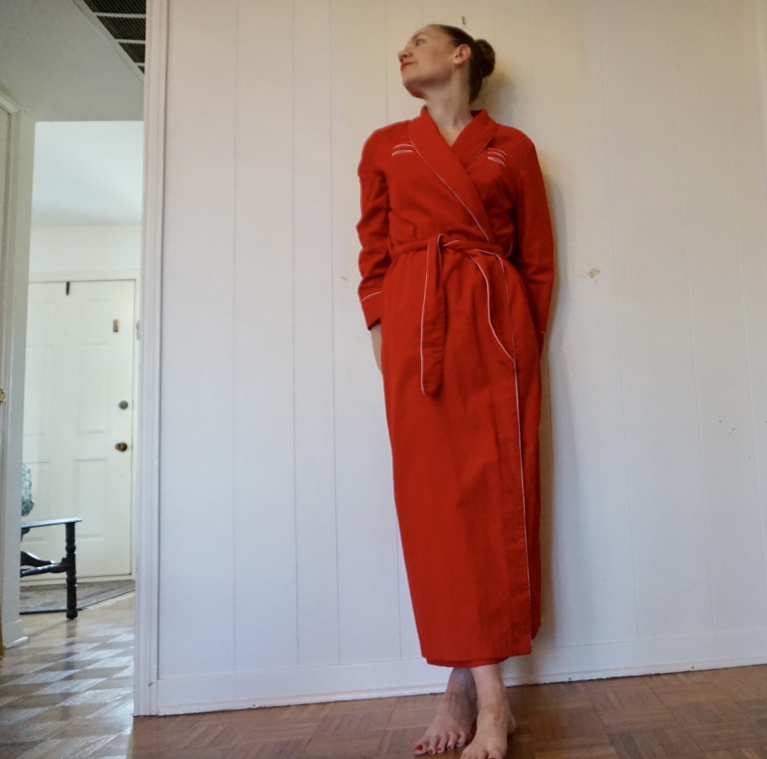 a woman in red corduroy robe against a white wall