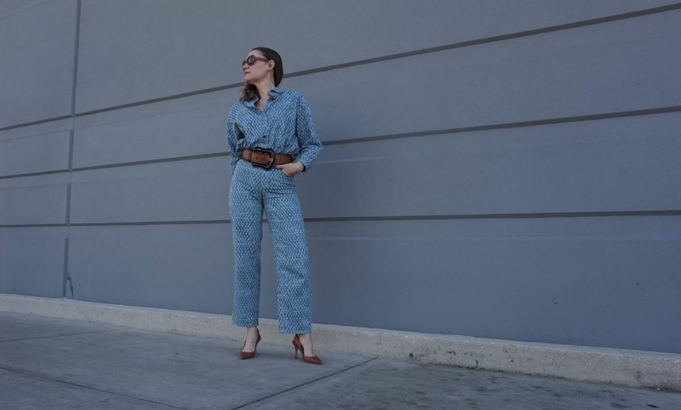 a woman in matching denim shirts and pants with a belt and sling backs in front of a concrete wall