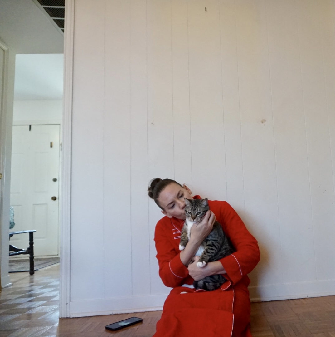 a woman in a red corduroy robe holding a cat by a white wall