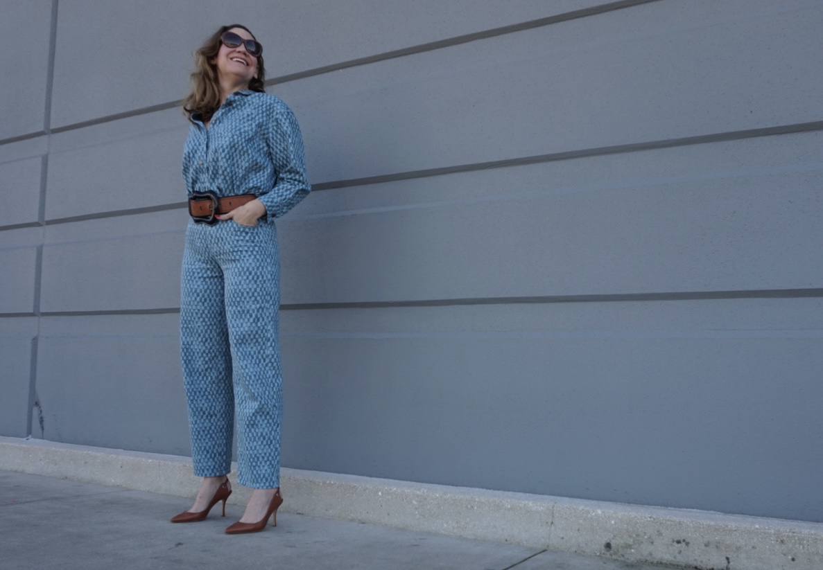 a woman in matching denim shirt and pants with belt and sling backs in front of a concrete wall
