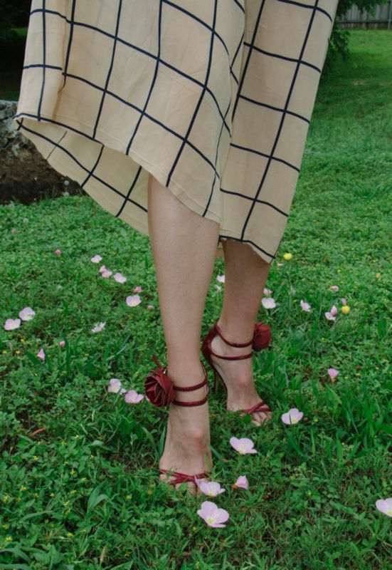 close up of red kitten heels with roses on the heel and legs in a nude and navy grid dress