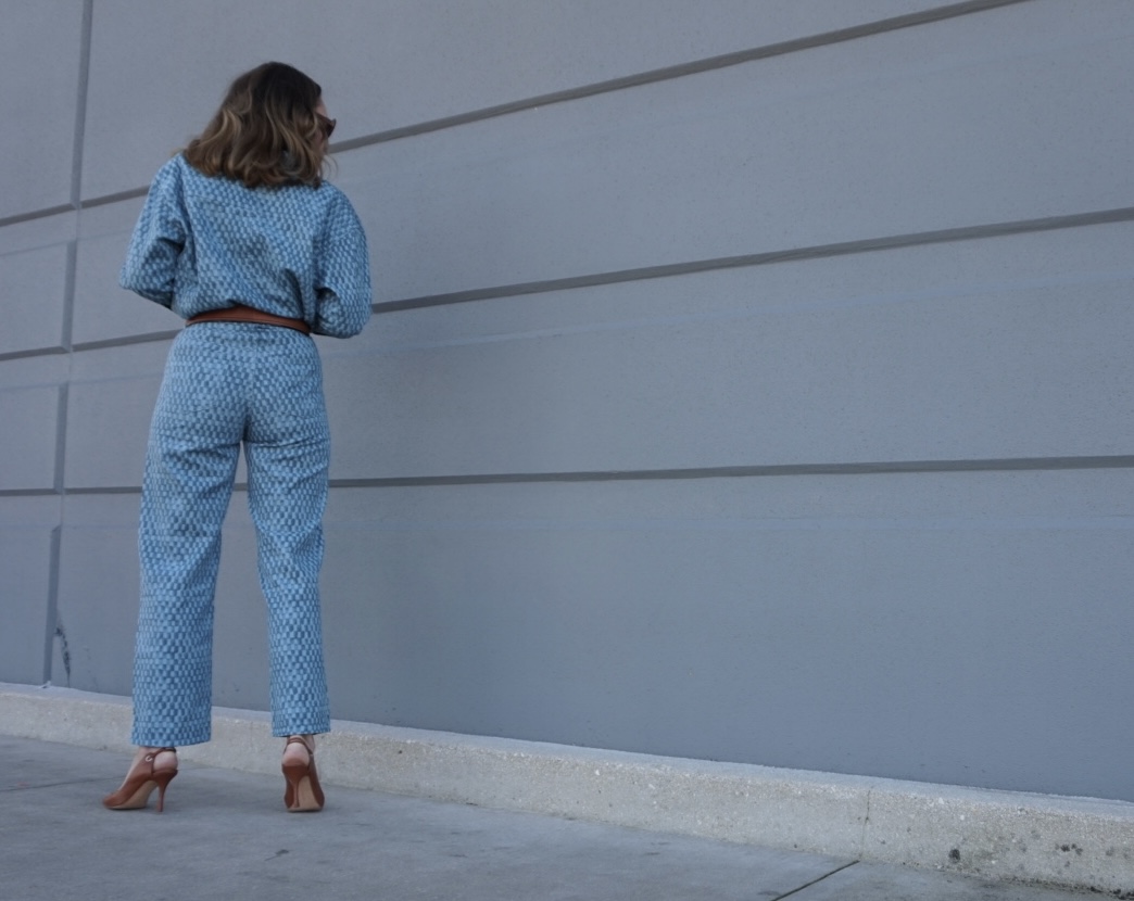a woman in matching denim shirt and pants, belt and sling backs in front of a concrete wall