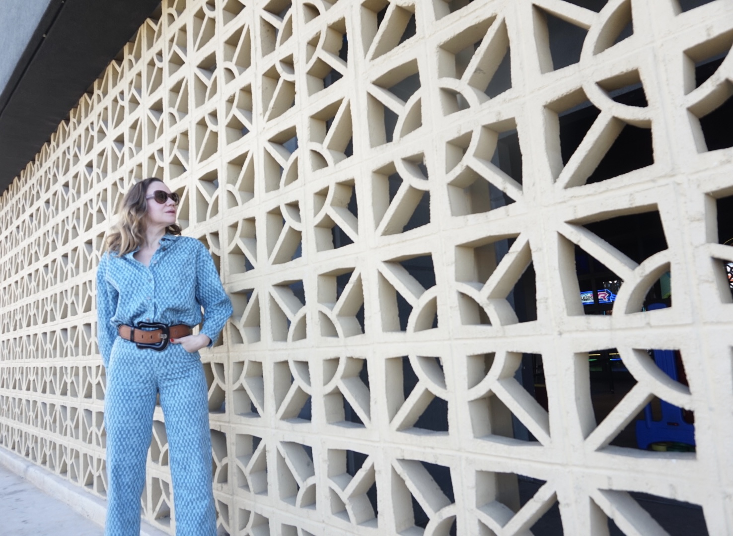 a woman in matching denim shirt and pants in front a concrete wall