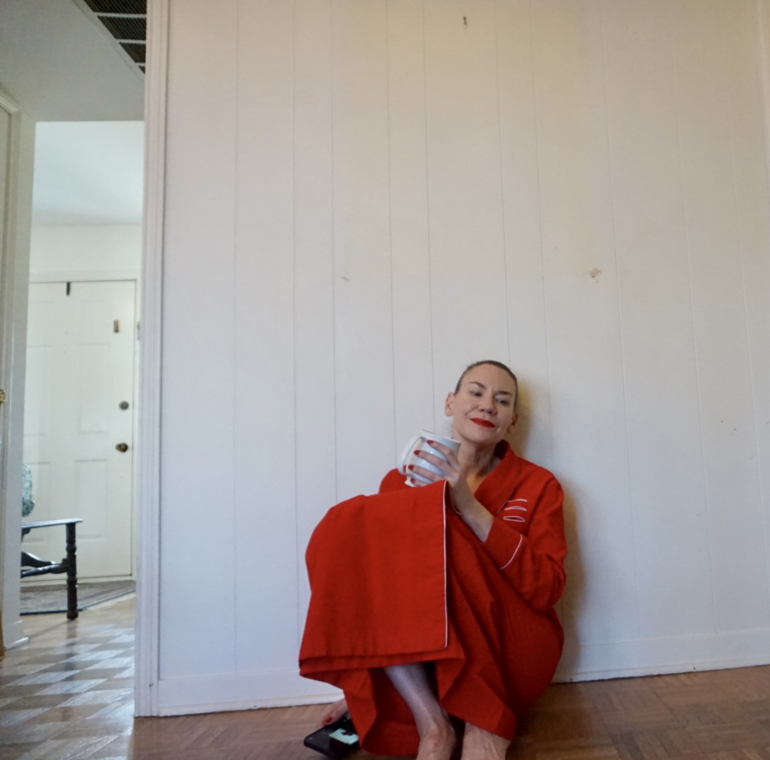 a woman in a red corduroy robe holding a white coffee mug against a white wall