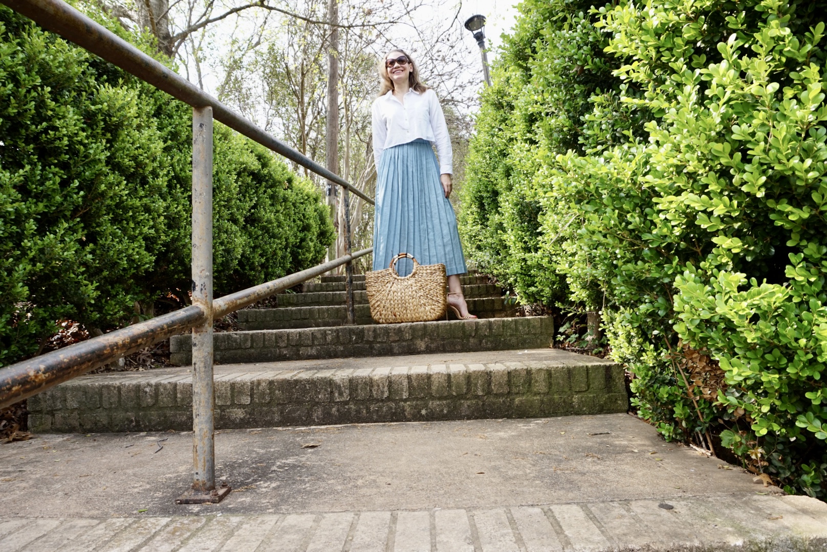 a woman in a cropped button down and blue pleated skirt on stairs