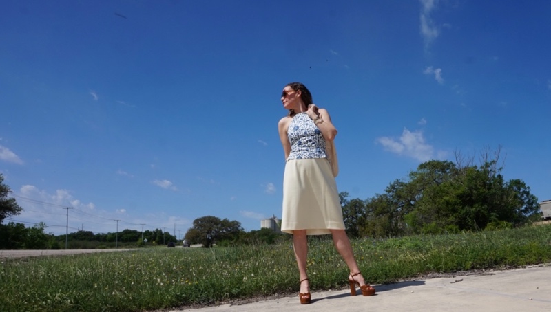 a woman in a blue and white top yellow skirt and brown shoes in a field of bluebonnets 