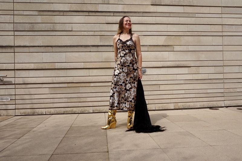 a woman in a black, gold and white slip dress with gold boots and a fringe shawl