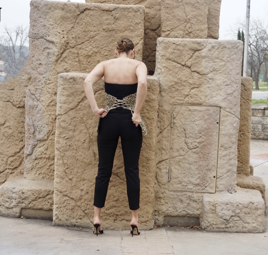 woman in black strapless top, pants, leopard corset in front of rock formation