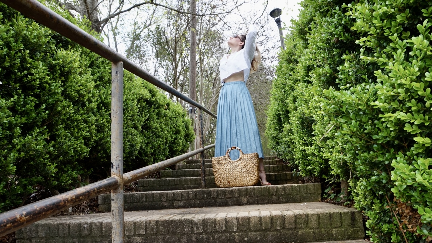 a woman in a cropped white button down and blue pleated mini skirt on stairs