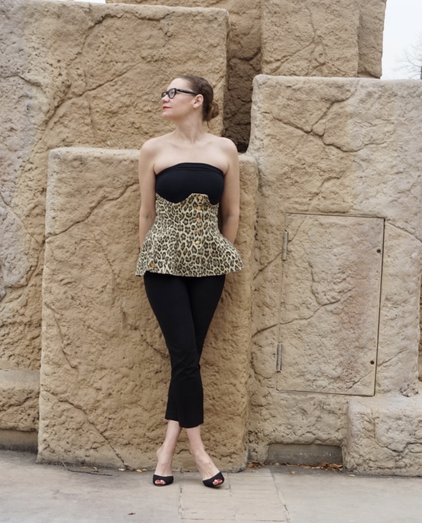 a woman in black strapless top, black pants, leopard corset in front of rock formations