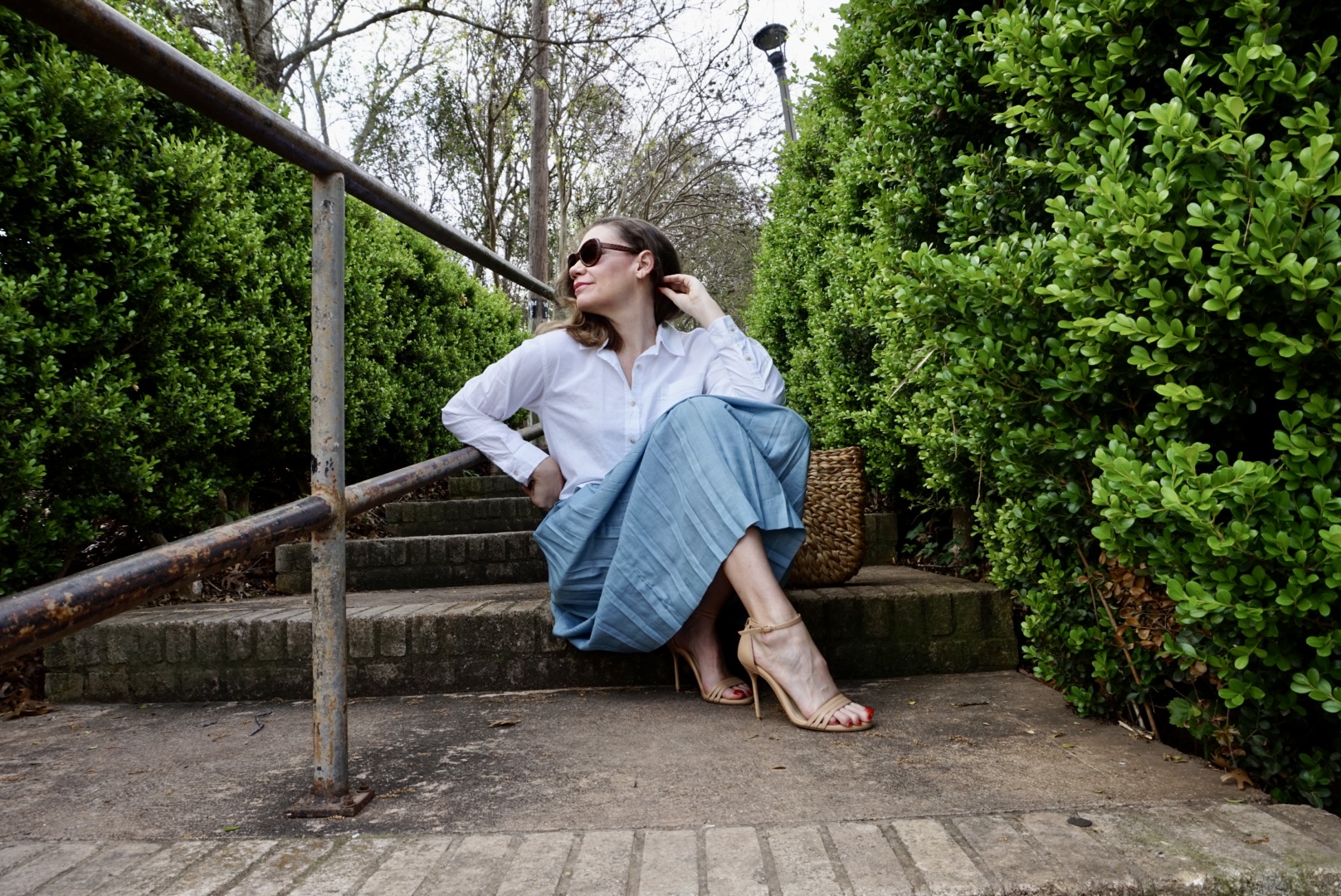 a woman in a cropped white button down and blue pleated skirt on steps
