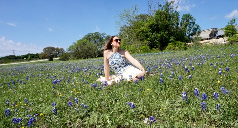 a woman in blue and white halter top and yellow skirt in a field if bluebonnets