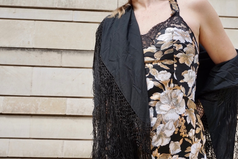 a woman in a black, gold and white slip dress with a fringe shawl