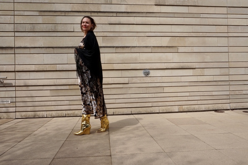 a woman in a black, gold and white slip dress, fringe shawl and gold boots