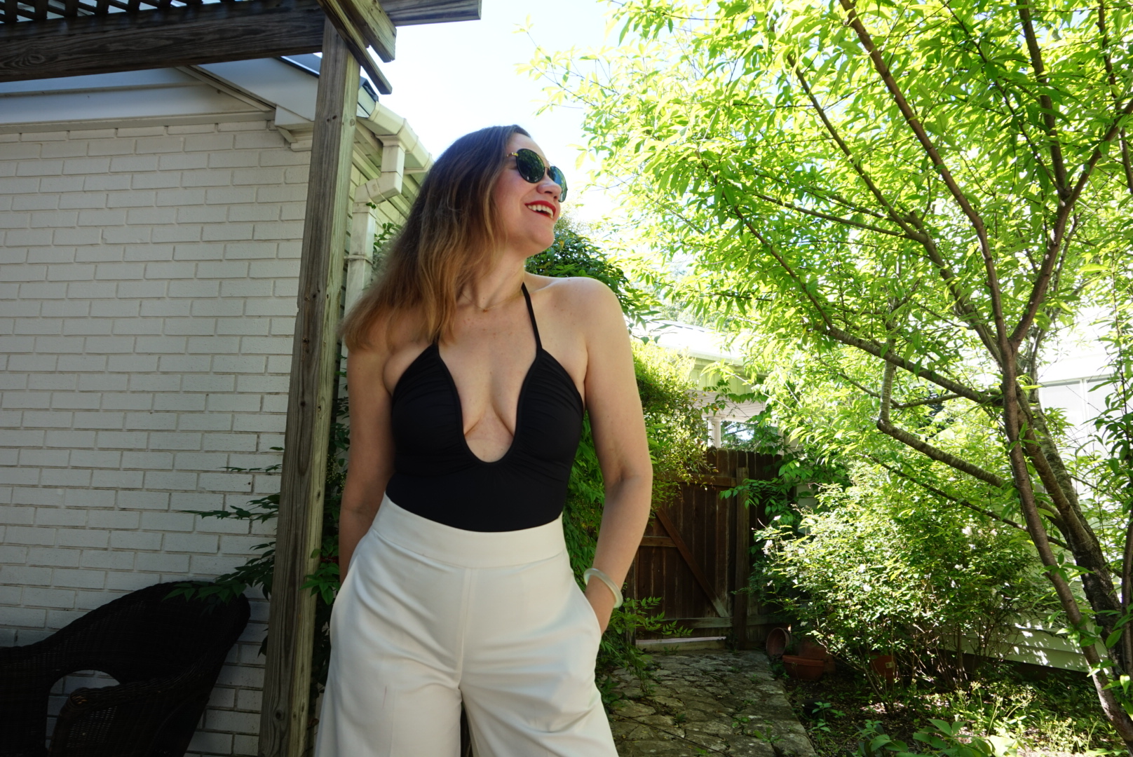 a woman in a low cut black swim suit and white pants in a garden