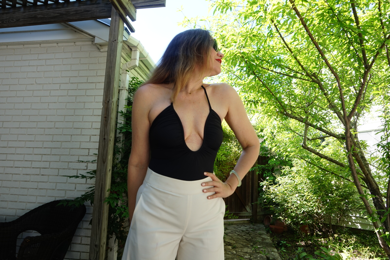 a woman in a low cut black one piece swimsuit and white pants in a garden