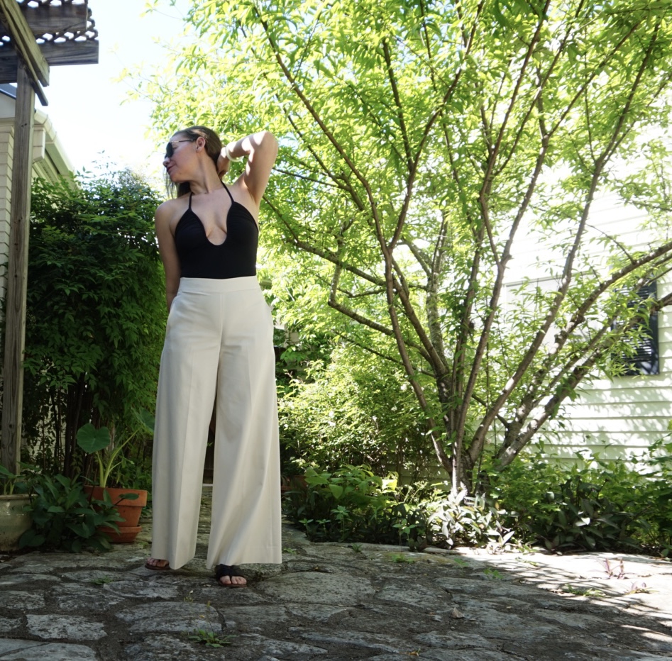 a woman in a low cut black swimsuit and white pants in a garden