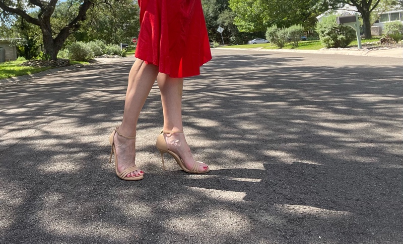 a woman in nude high heel sandals and the hem of a red dress in the middle of the road