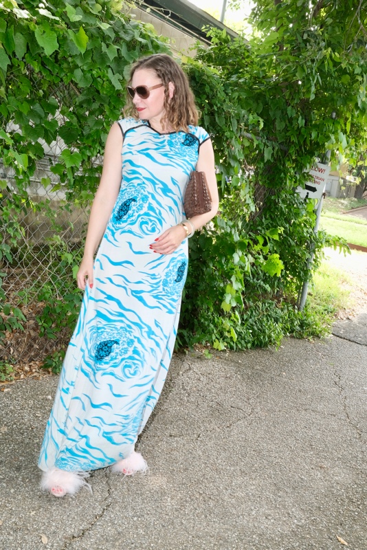 a woman in a blue and white floral slip dress with pink feather shoes and brown leather clutch 