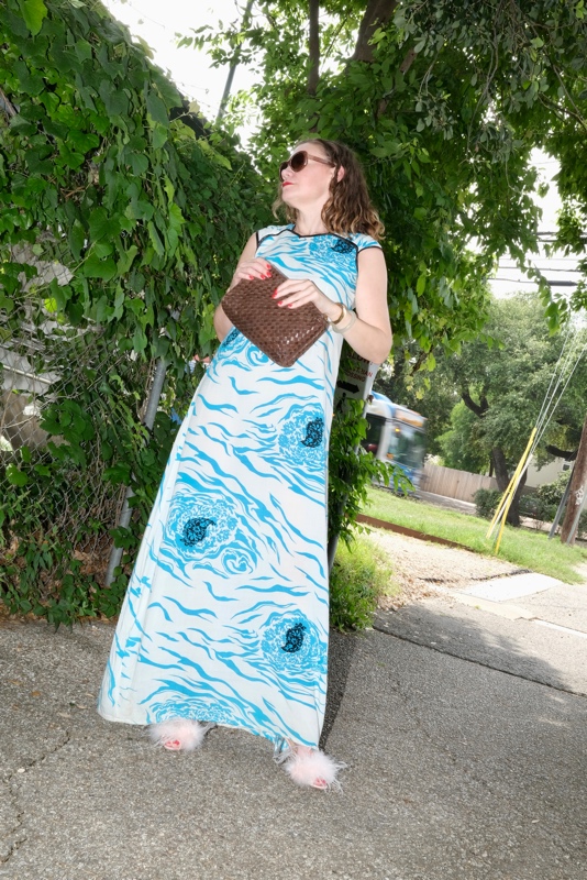 a woman in a blue and white floral slip dress with pink feather shoes and a brown clutch bag