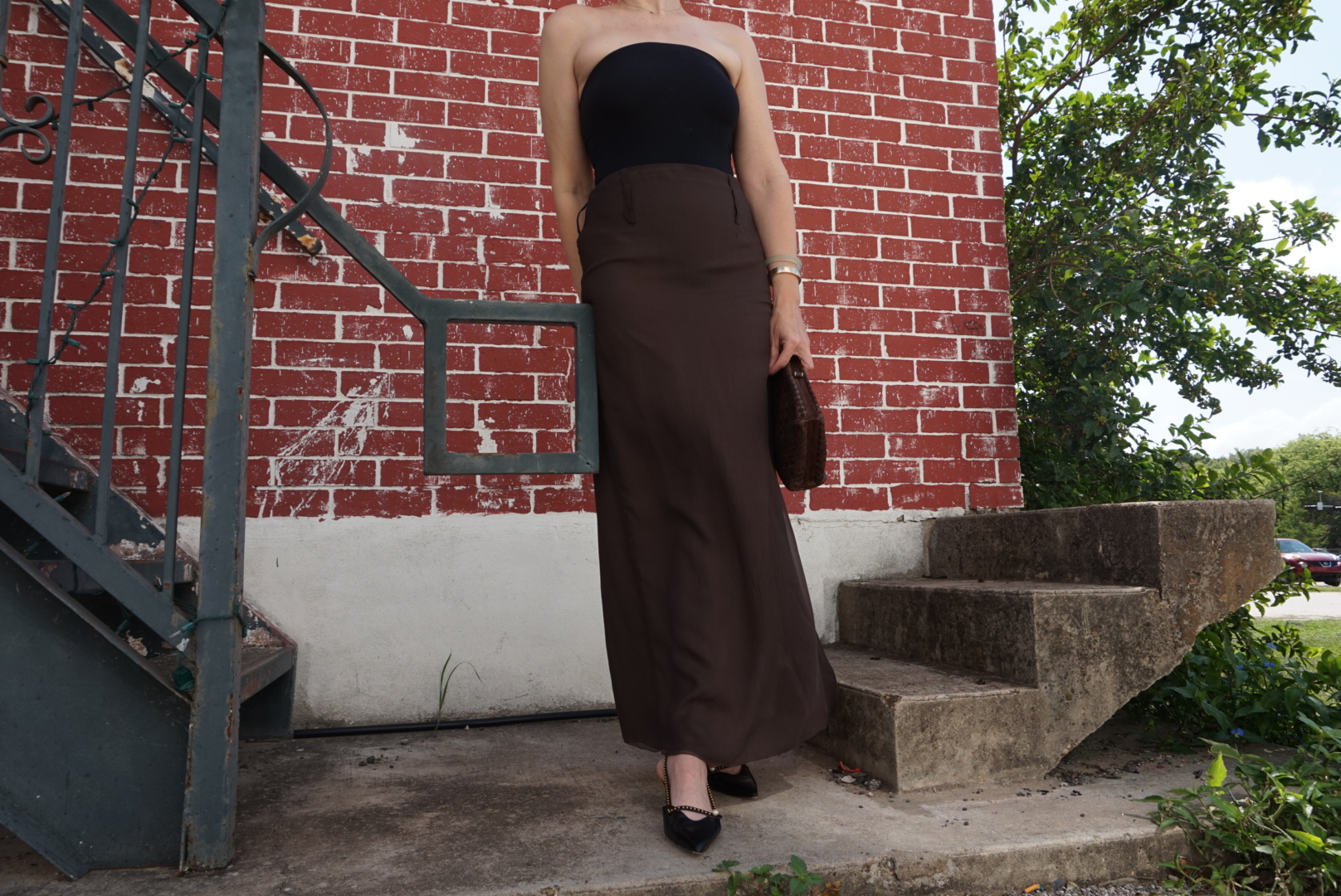 a woman in a black body suit, brown silk skirt, black kitten heels and a woven clutch