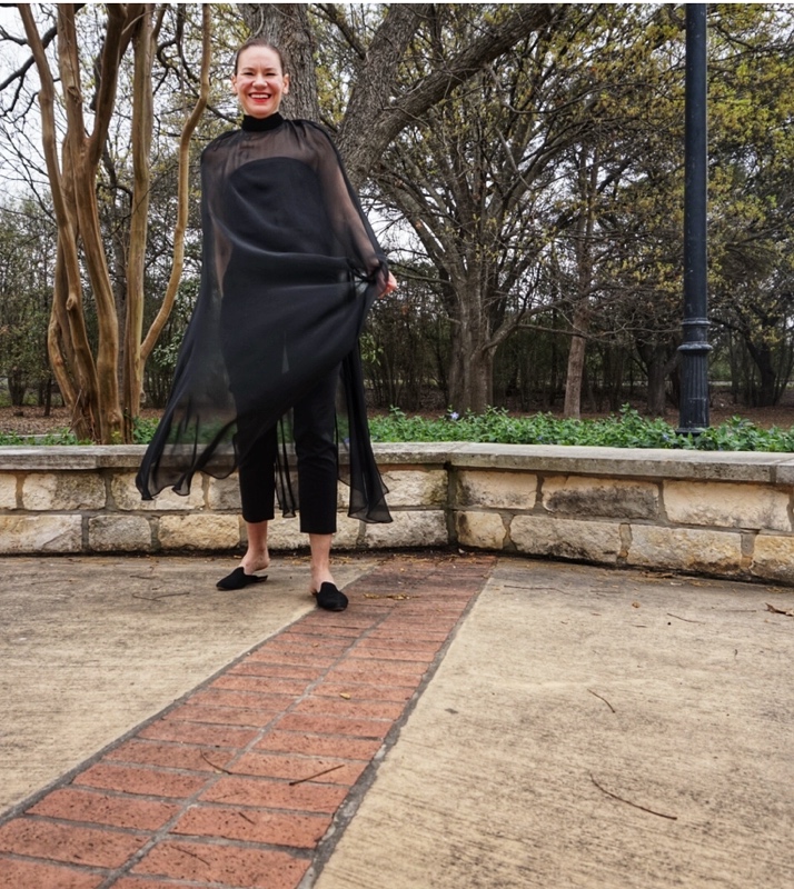 a woman in a strapless black top, black pants with black sheer cape over it and black mules