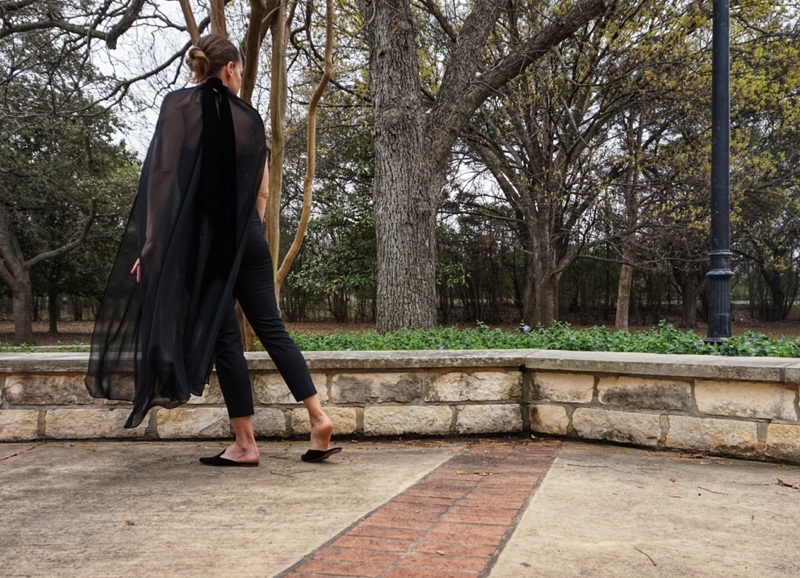 a woman in a strapless black top and black pants with a black sheer cape over it and black mules 