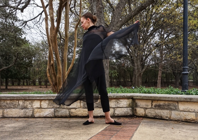 a woman in a strapless black top and black pants with a sheer black cape over wearing black mules