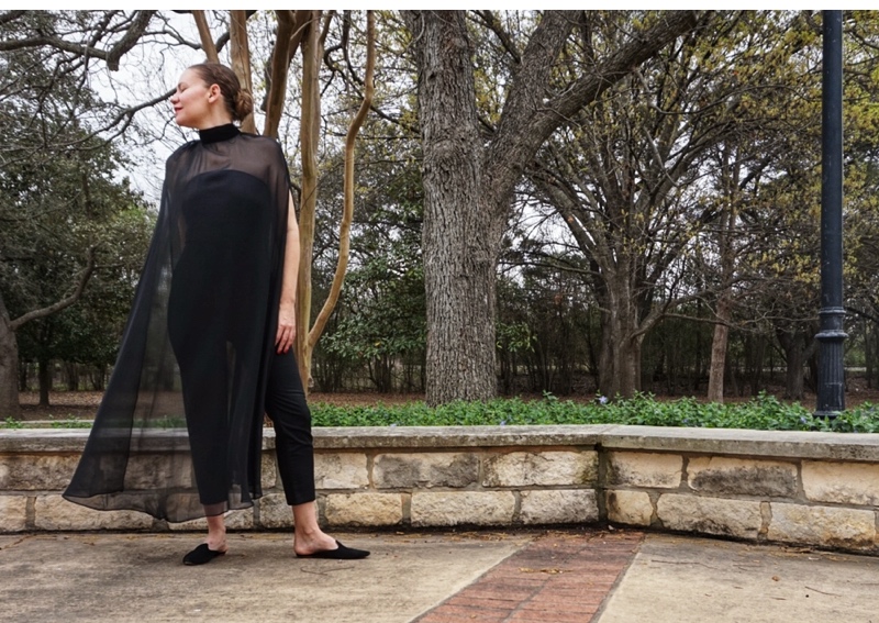 a woman in a strapless black top and black pants with a black sheer cape over and black mules