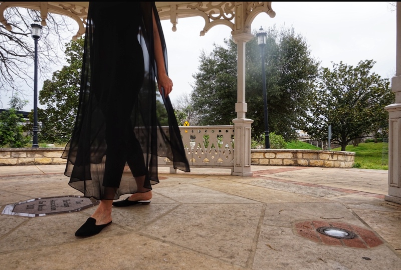 a woman in black pants with a black sheer cape and black mules