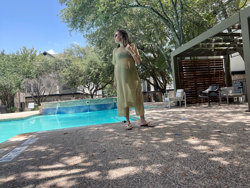 a woman in a black bandeau bikini under a gold sheer tunic and pant in front of a pool 