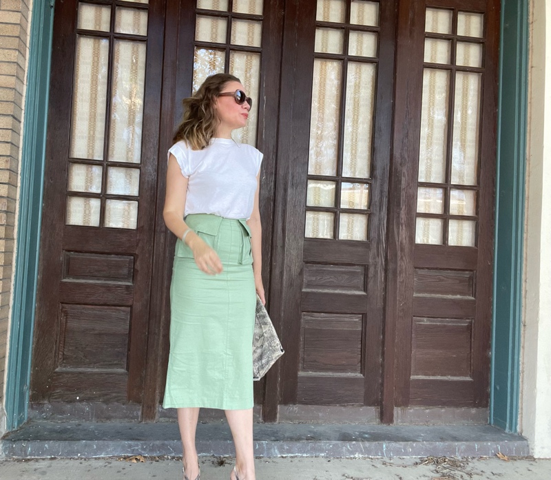 a woman in a green midi skirt with pockets, a white tee and snake purse, sunnies and shoes 