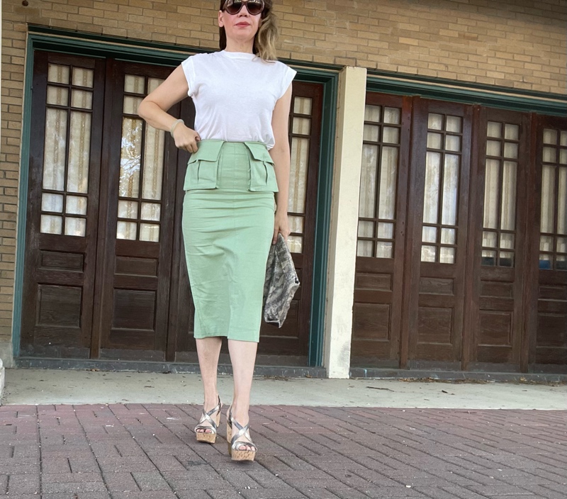 a woman in a green skirt and white tee and snake bag and wedges